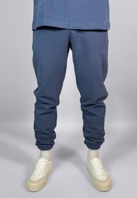 Kleita navy zili joggeri, kas izgatavoti no maigas auduma, ar elastīgiem piedurkņu galiem, sānu kabatām un brīvu pieguļumu, valkāti ar baltām platformas sneakerām.