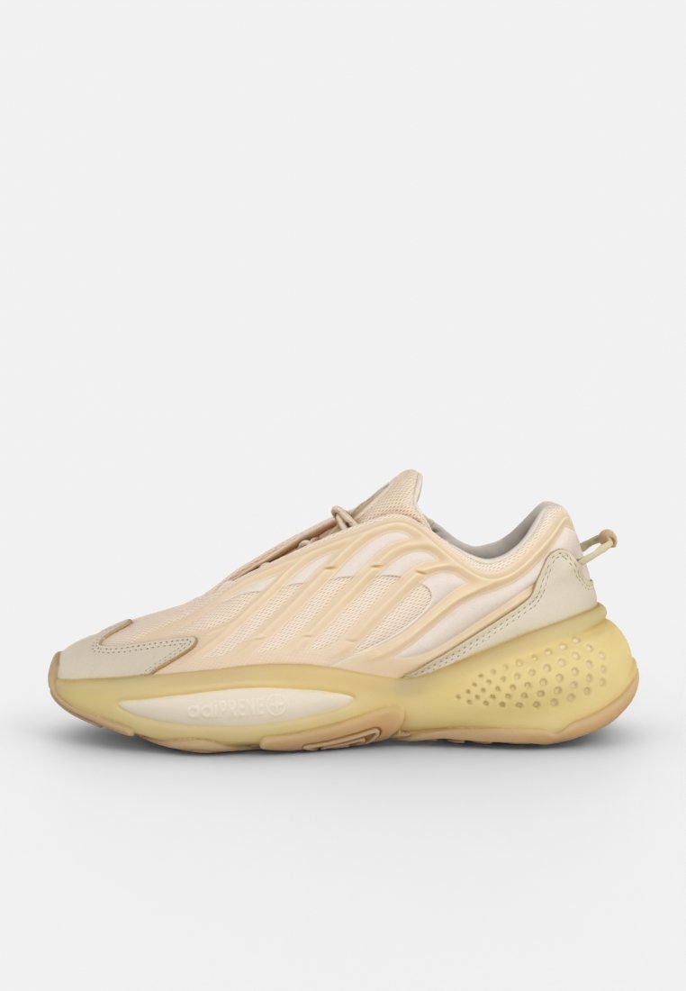 Zapatilla de color beige claro con textura de malla, diseño acanalado, suela curva y características de amortiguación integradas. Detalles en colores suaves y apagados.