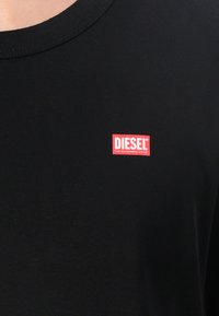 Sort T-shirt lavet af bomuld med ribbet rund hals. Har et rødt rektangulært Diesel-logo på brystet med hvid tekst.