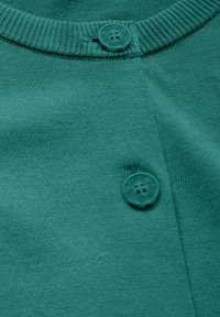 Tee-farbenes Baumwollstrickkleidungsstück mit einem runden, gerippten Halsausschnitt, das einen auffälligen dunkeltee-Farbenen Knopf und eine glatte Textur aufweist.