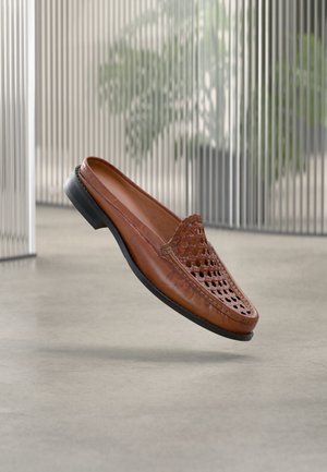 Chaussure à enfiler en cuir marron avec un design perforé, pied arrondi et semelle en caoutchouc noire. Tige texturée avec un détail subtil de couture.