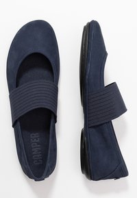 Paire de chaussures bleu marine à enfiler avec de larges bandes élastiques sur le dessus et des semelles plates noires, vues de dessus et de côté.