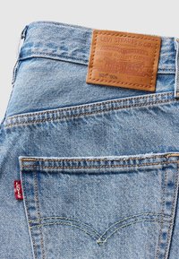 Poche arrière d’un jean Levi’s bleu clair avec un patch en cuir marron de la marque et une étiquette en tissu rouge Levi’s sur la couture latérale.