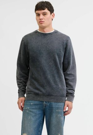 Sweatshirt gris foncé en tissu doux, avec un col rond et des poignets côtelés. Porté avec un jean en denim déchiré, mettant en avant un style décontracté.