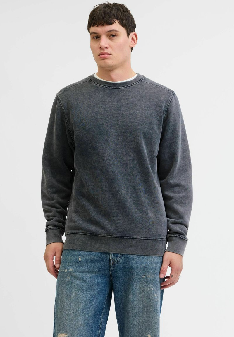 Donkergrijze sweatshirt van zachte stof, met een ronde hals en geribde manchetten. G gedragen met versleten denim jeans, wat een casual stijl benadrukt.