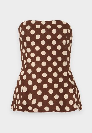 Donna che indossa un top peplum marrone senza spalline e pantaloni corti con grandi pois beige, abbinati a ballerine beige con punta.