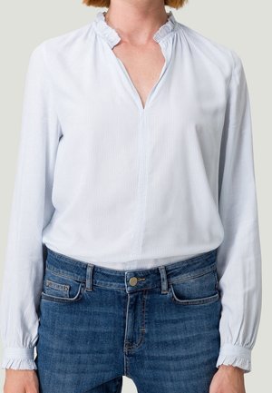 Blouse à rayures bleu clair avec un col à volants, des manches longues et des poignets froncés, associée à un jean bleu foncé. Texture douce et coupe décontractée.