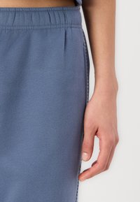 Helle blaue Jogginghose aus weichem Material, mit einem elastischen Bund und seitlichen Nähten. Eine Hand liegt auf dem Stoff.