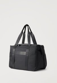 Μαύρη ορθογώνια τσάντα duffel με διπλούς ιμάντες μεταφοράς και πλαϊνή τσέπη με φερμουάρ, τοποθετημένη σε ένα απλό φωτεινό φόντο.