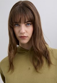 Olivgrön hoodie med mjuk textur, med en liten logotyp i mitten. Designen har en huva med dragsko och en avslappnad passform.