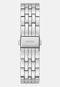 Srebrny metalowy zegarek na nadgarstek z bransoletą w formie ogniw. Posiada prostokątną klamrę z wygrawerowaną nazwą marki "GUESS". Gładka, błyszcząca powierzchnia.
