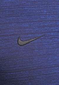 Maglietta sportiva Nike in tessuto blu scuro con un motivo strutturato; presenta un piccolo logo swoosh ricamato di colore nero sul petto.