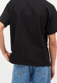 Camiseta de algodón negra de corte holgado, con mangas cortas y escote redondeado, combinada con jeans de mezclilla azul claro.