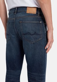 Jeans in denim blu scuro con una vestibilità dritta, leggere scoloriture e un'etichetta in pelle applicata sulla parte posteriore in vita, dotati di due tasche posteriori.