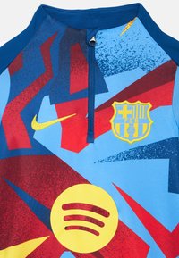 Maglia sportiva blu, rossa e gialla con mezza cerniera e maniche lunghe; presenta un logo Spotify e uno stemma ricamato del FC Barcelona.
