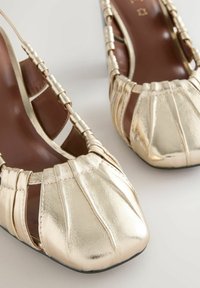 Gold metallic open-toe sandals with gathered detailing and beaded straps on brown insoles, placed on a light background.