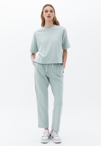 Licht muntgroen loungewear-set van zacht materiaal. Het topje heeft een ontspannen pasvorm met korte mouwen; de broek heeft een elastische tailleband en zijzakken.