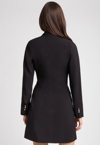 Czarna dopasowana sukienka z długimi rękawami, zrównoważona sylwetka, mankiety zapinane na jeden guzik i gładki materiał. Posiada czysty design z tyłu.