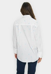 White shirt with light blue heart pattern, long sleeves, button cuffs, and a slightly curved hem. Soft, lightweight fabric, classic collar design.