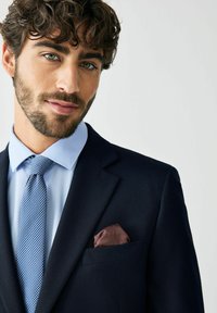 Marineblauer Anzug mit strukturiertem Finish, hellblauem Hemd, blau gemustertem Krawatte und einem kastanienbraunen Einstecktuch in der Brusttasche.