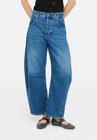 Jeans in denim blu a gamba larga con vita alta, caratterizzati da zone sbiadite, tasche frontali e cuciture a contrasto.