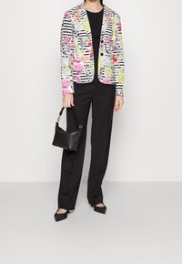Mehrfarbige Blazer mit Blumen- und Streifenmustern, getragen über einem schwarzen Oberteil und kombiniert mit schwarzen Hosen und einer kleinen schwarzen Handtasche.