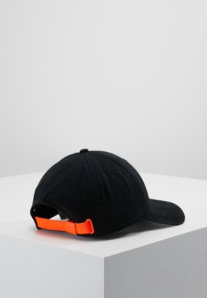 Czarna czapka z daszkiem z zakrzywionym rondem, regulowany jasnopomarańczowy pasek i przeszywane otwory wentylacyjne, umieszczona na białej powierzchni.