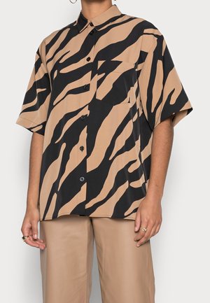 Kortærmet skjorte med knapper og sorte og brune tigerstriber, båret sammen med brune bukser, med en brystlomme og løs pasform.