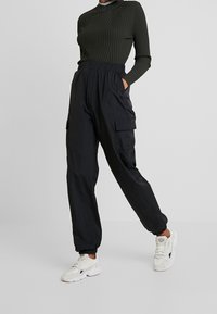 Zwarte, lichtgewicht cargobroek met elastische boorden en twee zijzakken. Gecombineerd met een lange mouw, geribd groen shirt en witte sneakers.