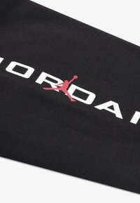 Mustast kangast, millel on sile tekstuur, kujutades suuri valgeid tähti "JORDAN" ja punast hüppava kujuga siluetti.