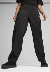 Zwarte cargobroek met een elastische tailleband, twee zijzakken en een strak ontwerp. De stof heeft een gladde textuur; gecombineerd met zwarte sneakers.