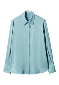Lyseblå langærmet skjorte lavet af glat stof. Har klassisk krave og knapfront, med let indsnorende manchetter og en rundet nederkant.