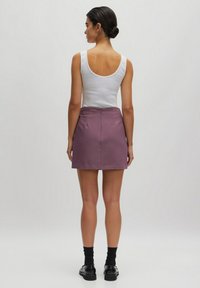 Paarse geplooide mini-rok met een rits aan de achterkant, gecombineerd met een witte tanktop. De outfit heeft een gladde textuur en een eenvoudig ontwerp.