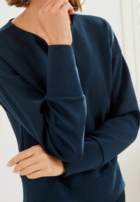 Sweat-shirt bleu marine en tissu doux, avec un col rond et des manches longues à poignets côtelés. Design simple et épuré.