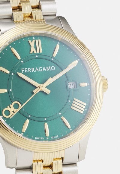 Gold and silver-tone watch with a green dial, Roman numeral XII, date display, and gold accents on hour markers and hands. Swiss-made.