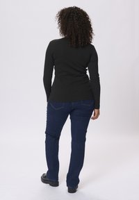 Un haut noir à manches longues associé à un jean en denim bleu foncé. La chemise a une coupe cintrée, et le jean présente une coupe classique avec un minimalisme dans les détails.