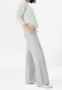 Pantalon de survêtement gris à jambes larges avec une taille élastique et des poches, associé à un haut à manches longues texturé de couleur claire.