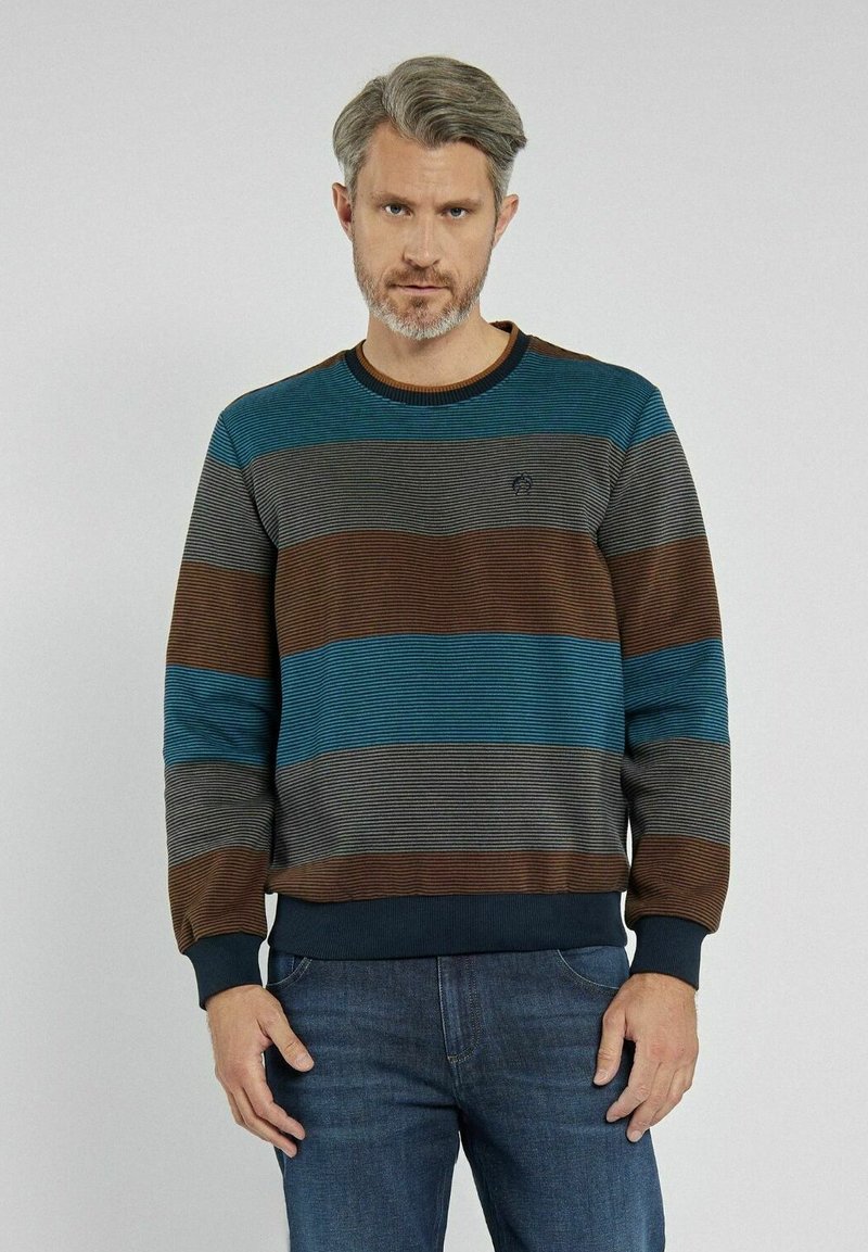 Sweter w paski w odcieniach teal, brązu i szarości. Żebrowany kołnierz i mankiety. Miękka tekstura z poziomymi paskami. Połączony z ciemnoniebieskimi dżinsami.