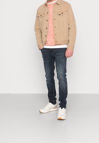 Vaaleansininen farkkutakki, vaalea vaaleanpunainen collegepaita, valkoinen t-paita, tummansiniset farkut ja valkoiset kengät, joissa on vaaleita yksityiskohtia.