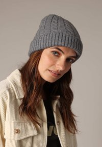 Grijze gebreide beanie met kabelbreiselontwerp en omgeslagen geribbelde manchet, gemaakt van zacht textiel; gecombineerd met een crèmekleurige corduroy jas.