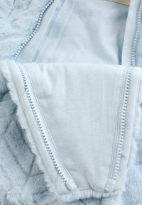 Helles blaues Kunstfell-Kleidungsstück mit einer glatten, weichen Textur. Verfügt über Kontrastnähte und einen Reißverschluss, die die Designmerkmale hervorheben.