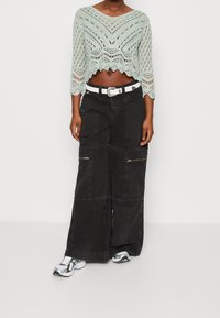 Svetle modrý háčkovaný crop top s vlnkovaným lemem; černé cargo kalhoty s mnoha kapsami a zipy; bílý pásek a stříbrné tenisky.