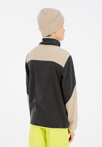 Fleecejack met hoge kraag in zwart en beige, met een color-block ontwerp. Combinatie met een beige gebreide beanie.