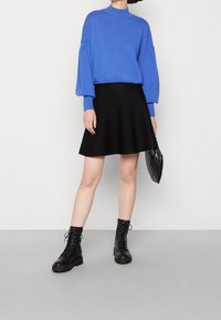 Blauer Strickpullover mit hohem Kragen, schwarzer ausgestellter Rock, schwarze Stiefeletten und eine schwarze gesteppte Tasche. Glatte Textur, lässiges Design.