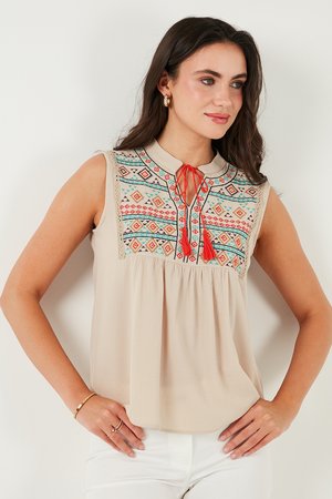 Beige sleeveless blouse with a collar, featuring multicolored geometric embroidery at the yoke and a tie-detail neckline. Lightweight fabric.