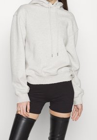 Světle šedá oversized mikina s klokaní kapsou, kapucí na stažení a žebrovanými manžetami, doplněná černými šortkami a koženými botami po kolena.