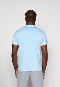 Hellblaues kurzärmeliges T-Shirt, Rundhalsausschnitt, glatte Textur, figurbetonte Form, getragen mit grauen Hosen. Geeignet für Freizeitkleidung oder zum Sport.