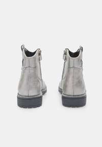 Botines metálicos plateados hasta el tobillo con un acabado liso, cierre de cremallera, tacón texturizado y suela de goma negra contrastante. Acentos de costuras reforzadas.