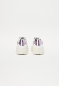 Weiße Sneakers mit lila metallic Akzenten an der Ferse, glatte Textur und einer klobigen Sohle. Entwickelt für Komfort mit abgerundeten Kanten.
