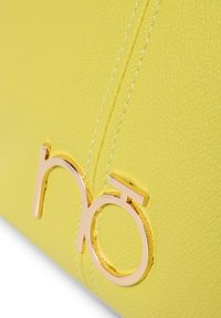 Geel getextureerde leren handtas met een prominent gouden logo-accent en zichtbare stiksels.